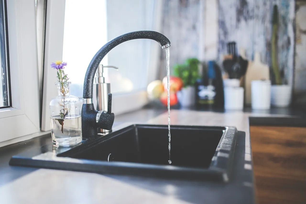 Black kitchen faucet running water into a dark stone sink